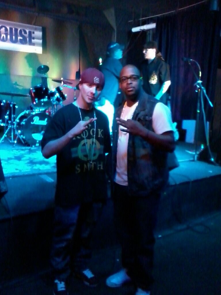 TakTrack and a friend posing in front of a stage with a drum kit under blue lights.