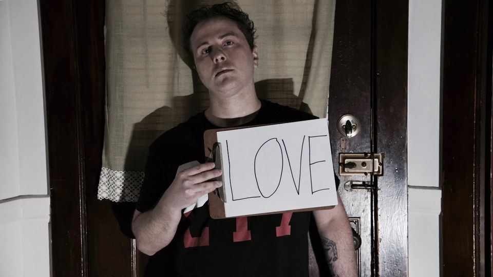 TakTrack holding a hand-lettered LOVE sign in a doorway.