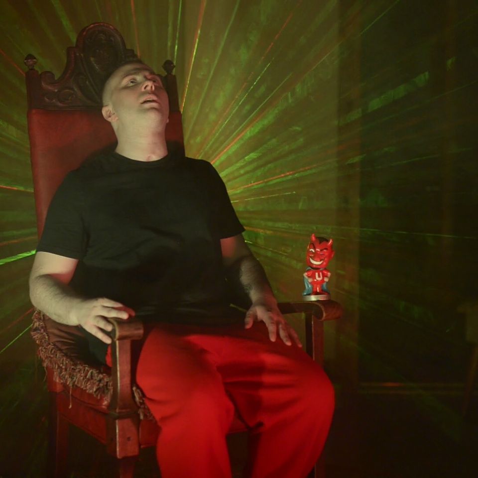 TakTrack sitting back in a carved red throne, green laser light fanning out behind him.